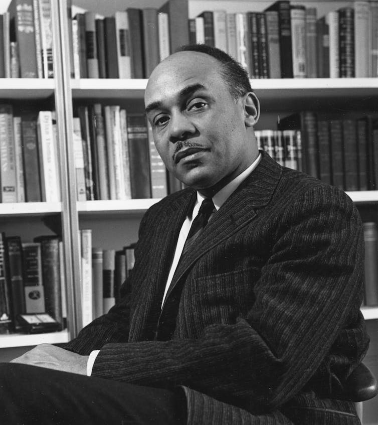 A black-and-white portrait of a man in front of a shelve of books.